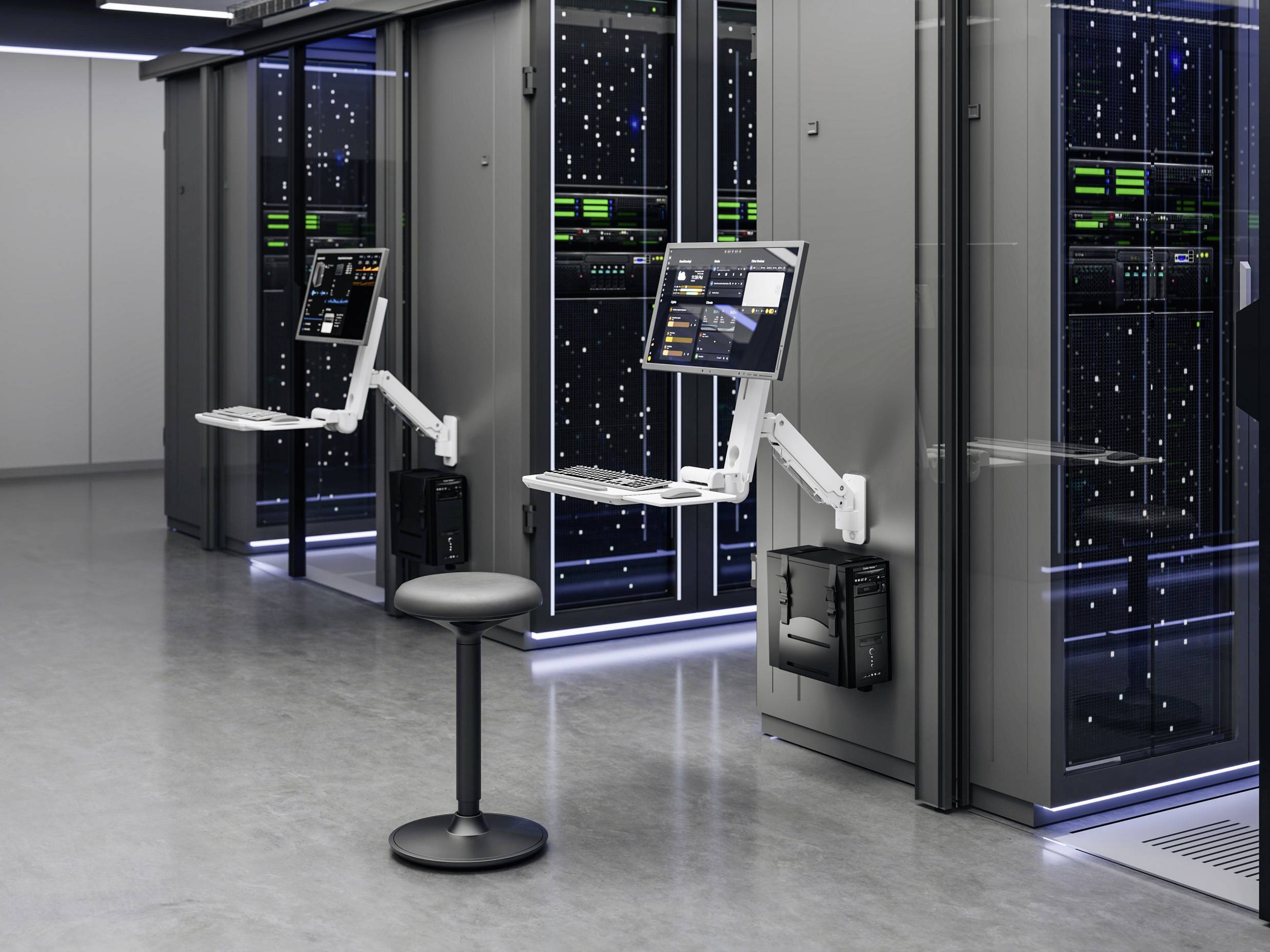 Nowoczesna serwerownia z wysokimi, przeszkloną obudową szaf serwerowych. Dwa stanowiska z monitorami, klawiaturą i myszką zamocowane na ramionach. W pobliżu ustawiony jest stołek.