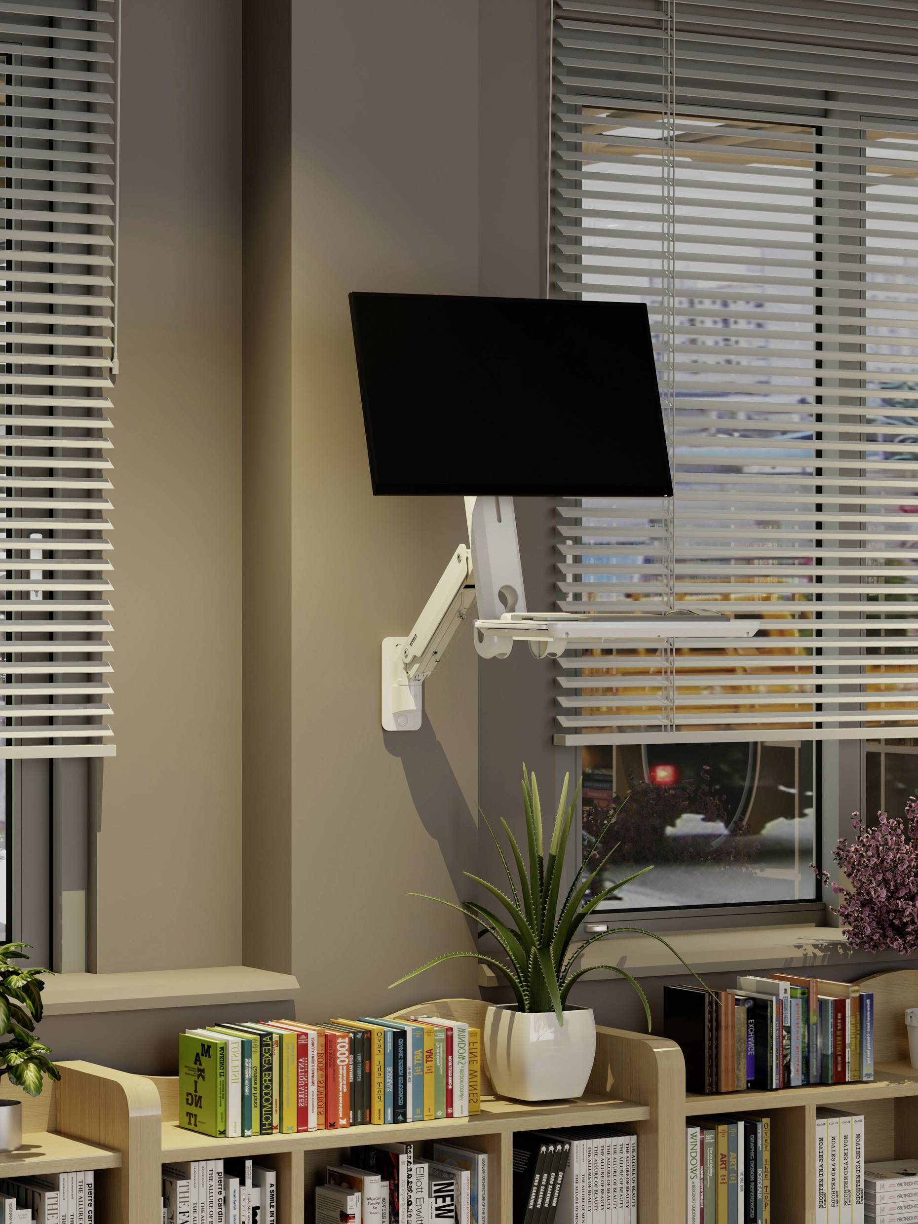 Monitor komputerowy jest zamontowany na regulowanym ramieniu przymocowanym do ściany nad regałem wypełnionym książkami i roślinami, obok okna z żaluzjami.
