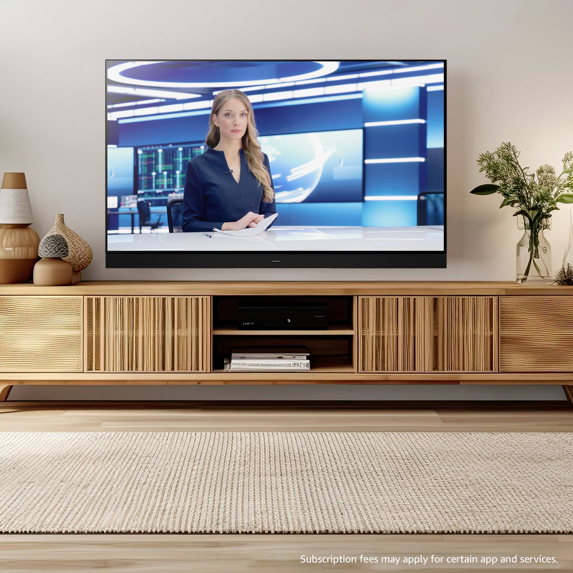 Nowoczesny salon z dużym telewizorem plazmowym, na którym wyświetlana jest transmisja wiadomości z prowadzącą. Na konsoli stoją ozdobne przedmioty.