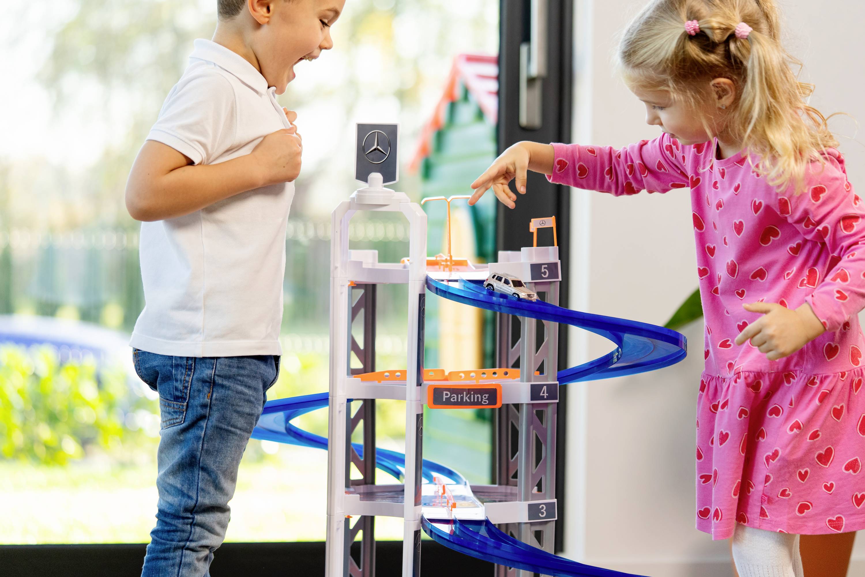 Chłopiec i dziewczynka z podekscytowaniem bawią się spiralnym torem parkingowym w pomieszczeniu. Chłopiec wygląda na zaskoczonego, gdy dziewczynka umieszcza samochodzik na torze.