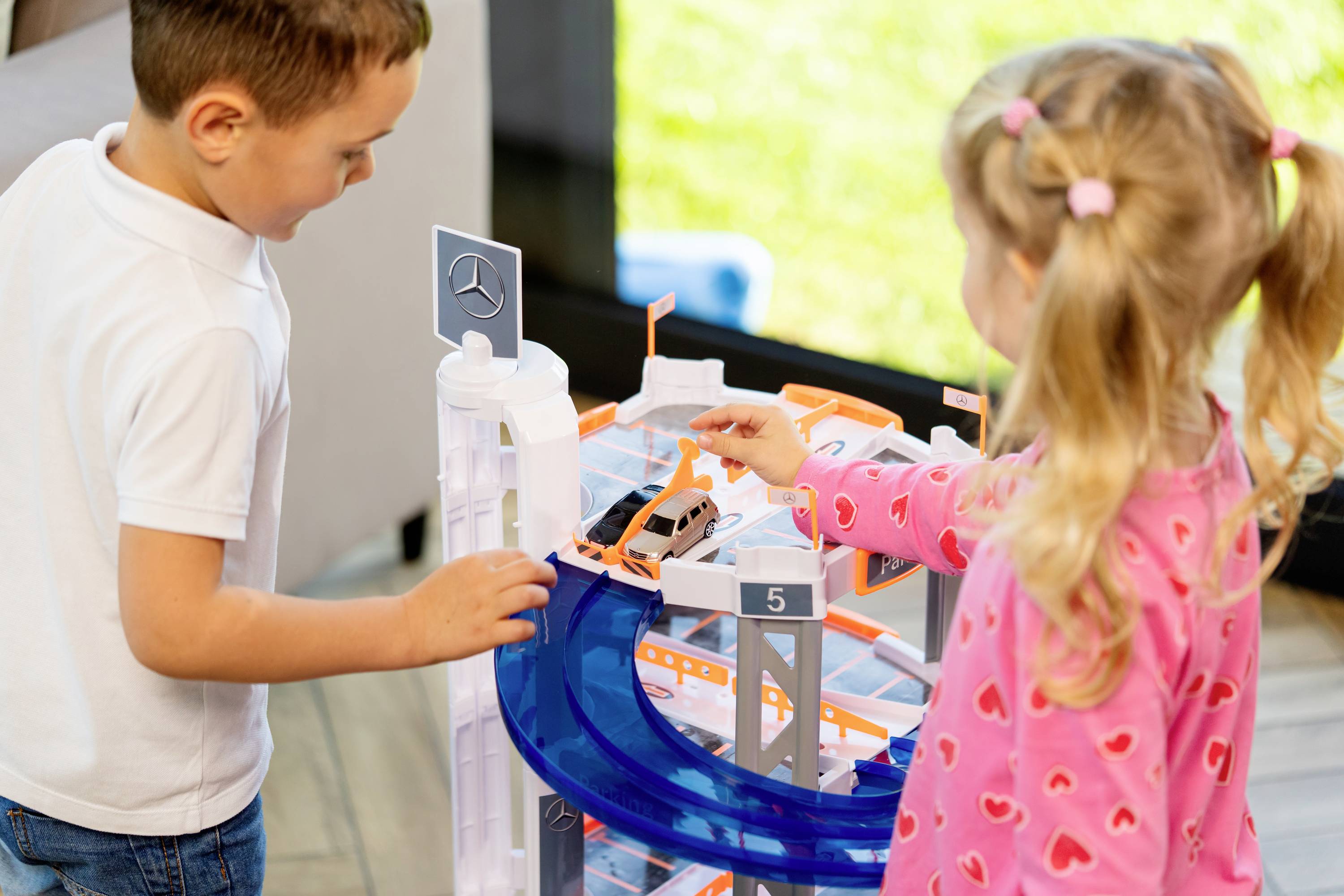 Dwoje dzieci bawi się torem wyścigowym, prowadząc samochodzik po niebieskiej pętli. Są całkowicie skupieni, wspólnie przeżywając radosną zabawę.