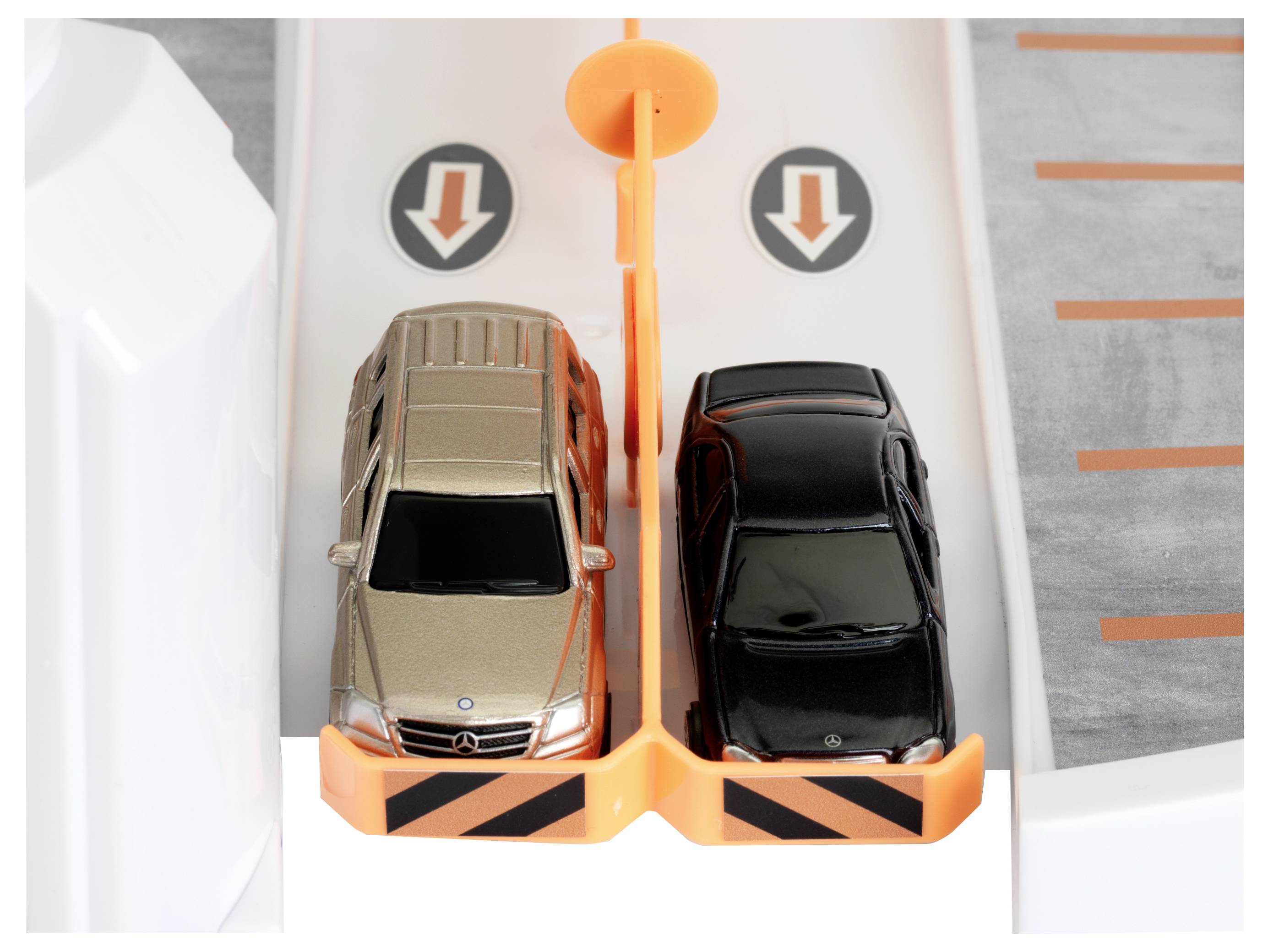 Dwa samochodziki zaparkowane obok siebie w miniaturowym parkingu, rozdzielone pomarańczową barierą. Strzałki kierunkowe wskazują w dół nad każdym samochodem.