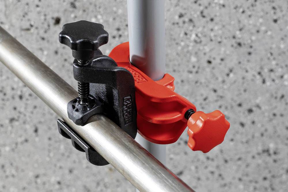 Czerwono-czarny metalowy zacisk mocuje dwie metalowe pręty prostopadle na betonowym tle.