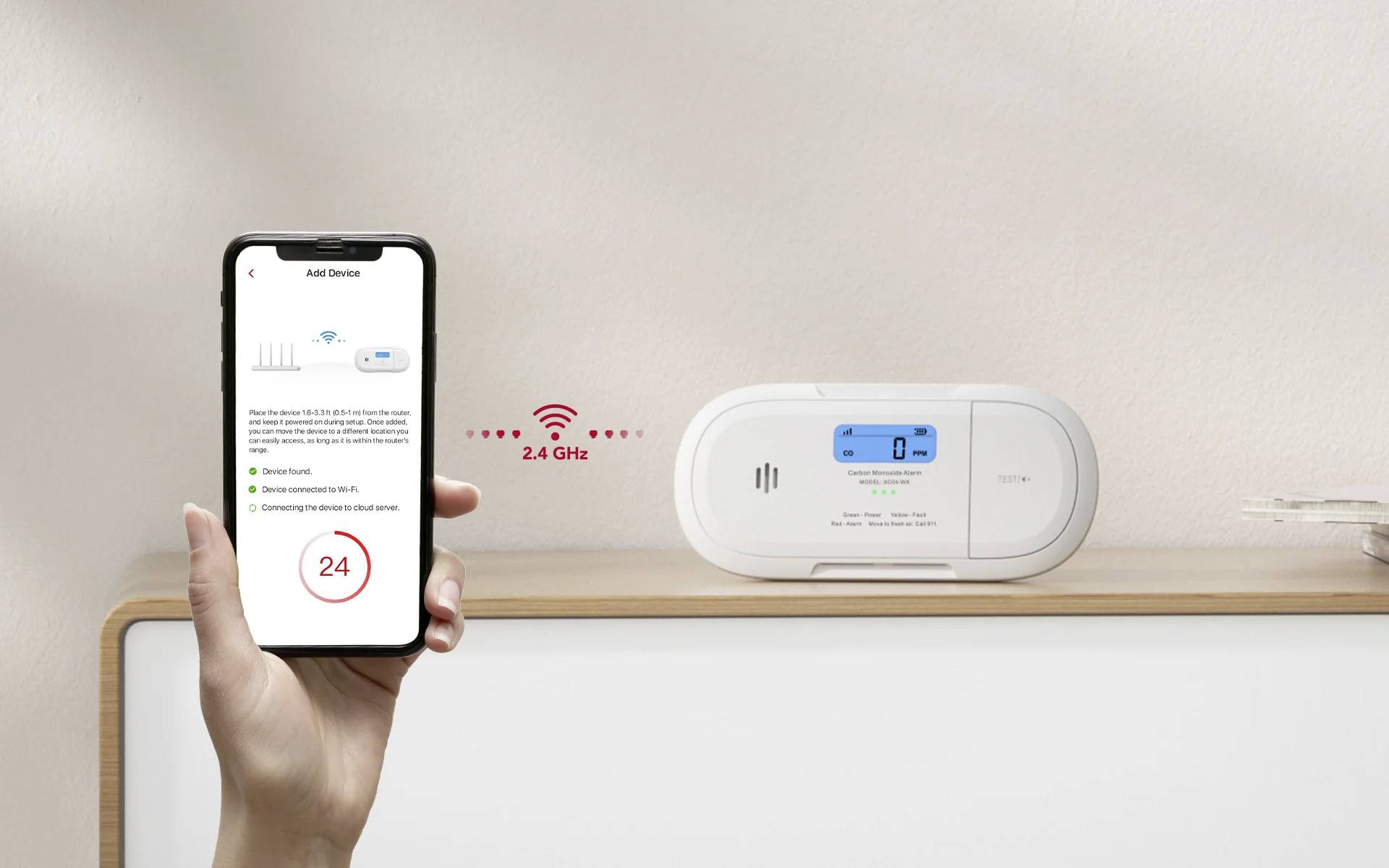 Dłoń trzyma smartfon wyświetlający ekran aplikacji inteligentnego domu. W pobliżu znajduje się urządzenie inteligentnego domu z cyfrowym wyświetlaczem pokazującym niebieski ekran. Ikona Wi-Fi wskazuje połączenie 2,4 GHz.