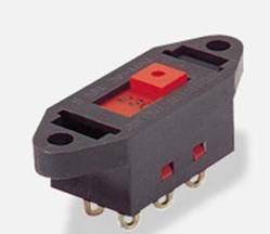 Mały czarny elektryczny przełącznik z czerwonym przyciskiem, wyposażony w piny lutownicze i otwory montażowe po obu stronach do instalacji.