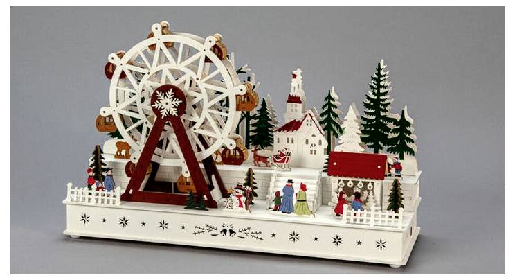 Drewniany model diabelskiego młyna z postaciami świątecznymi i drzewami, przedstawiający zimową scenę wiejską z ludźmi cieszącymi się atrakcją.