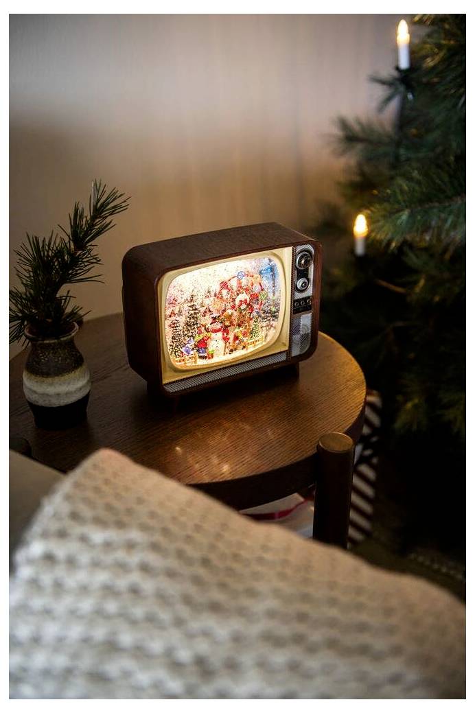Mały, zabytkowy telewizor z migoczącą świąteczną sceną wyświetlaną na ekranie stoi na stoliku bocznym w pobliżu przystrojonej choinki.