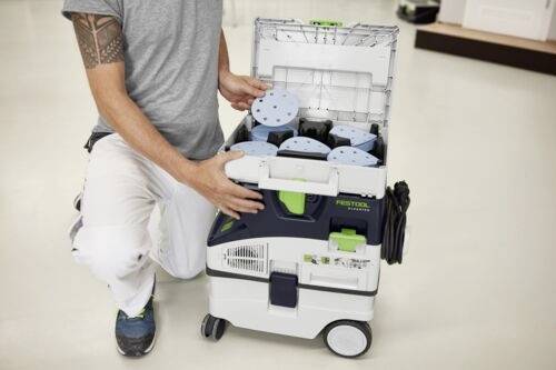 Osoba klęczy obok pojemnika na narzędzia z kółkami, organizując krążki ścierne w jego przegródkach.