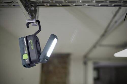 Przenośna lampa robocza wisi na metalowej szynie w garażu, oświetlając przestrzeń swoim jasnym paskiem LED.