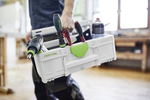 Osoba trzymająca skrzynkę narzędziową z różnymi narzędziami, w tym wiertarką i śrubokrętami, w otoczeniu warsztatu.