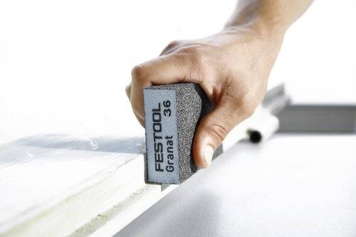 Dłoń trzyma blok szlifierski Festool oznaczony etykietą 'Granat 36', którym szlifuje krawędź powierzchni, wygładzając ją do wykończenia.