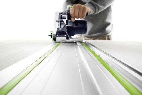 Osoba używa narzędzia elektrycznego do cięcia materiału wzdłuż zielonej prowadnicy, sugerując precyzyjną pracę.