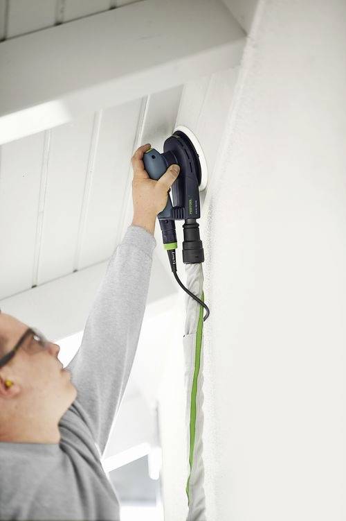 Osoba używająca ręcznej elektrycznej szlifierki do wygładzania wewnętrznej ściany, koncentrująca się na krawędzi sufitu.