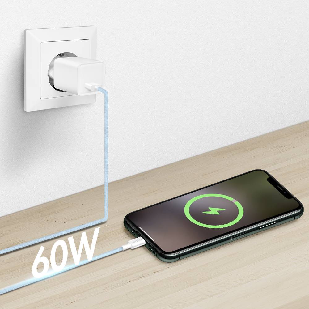 Smartfon ładuje się na drewnianej powierzchni, podłączony do gniazdka ściennego. Na ekranie widać symbol ładowania, a kabel jest oznaczony napisem '60W'.