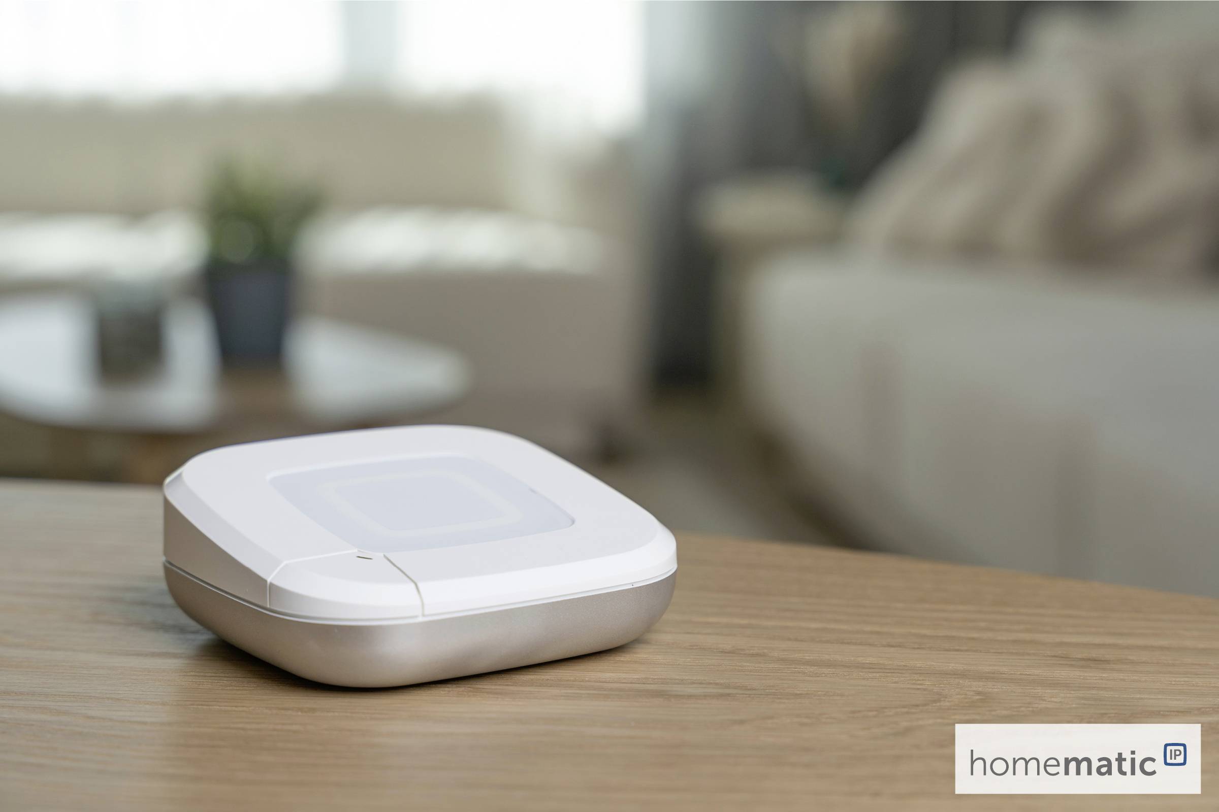 Inteligentne urządzenie domowe stoi na drewnianym stole w salonie. W tle widać rozmyte kanapy i roślinę, tworząc przytulną atmosferę.