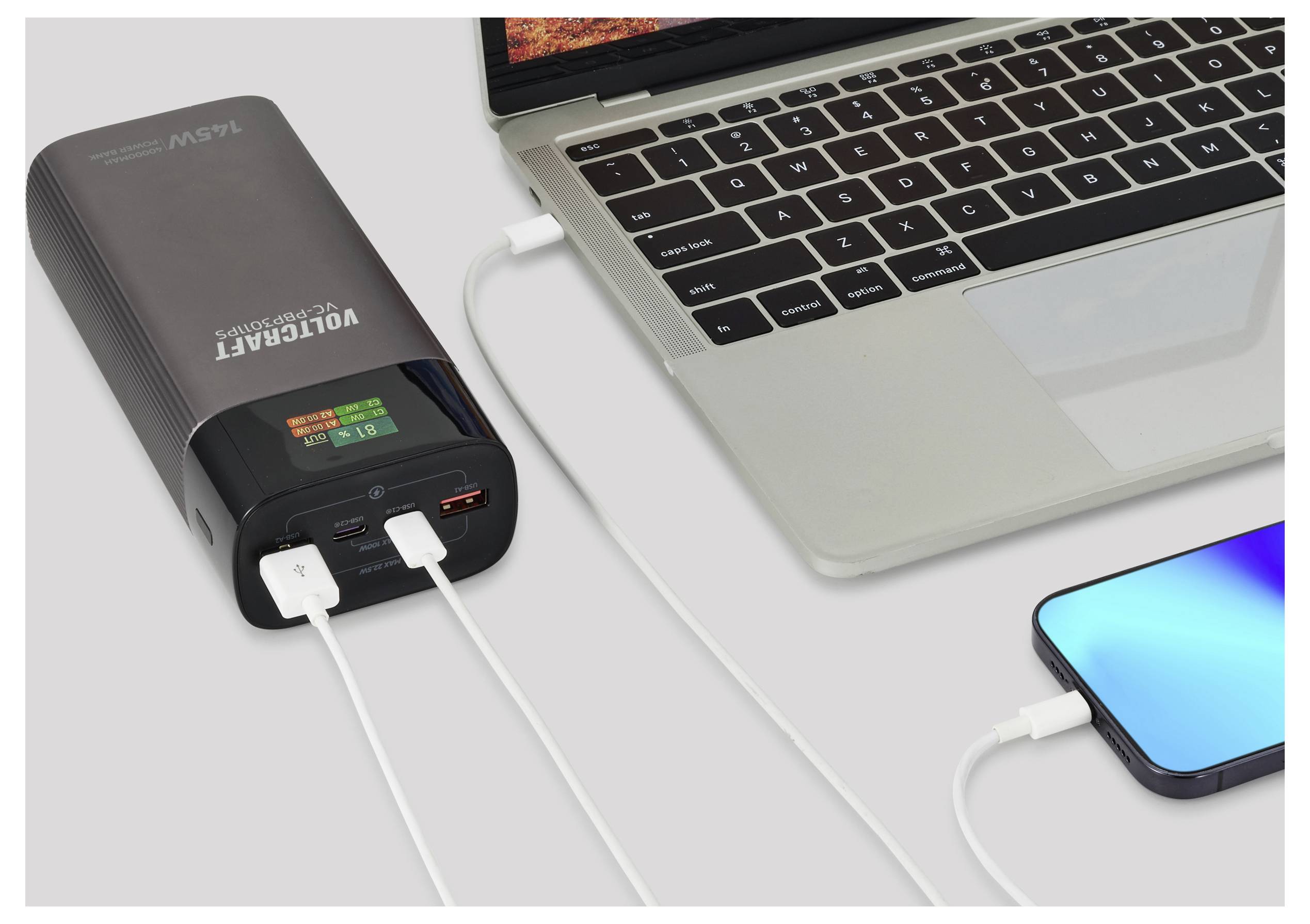 Powerbank ładujący jednocześnie laptopa i smartfona. Laptop jest włączony z otwartym ekranem, a telefon wyświetla niebieski ekran.