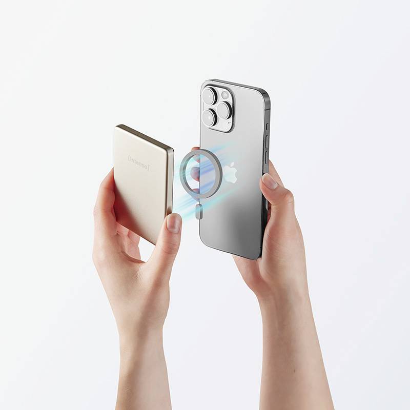 Dłonie trzymające srebrny smartfon i beżowy powerbank, ustawiające je do ładowania bezprzewodowego z widoczną animacją ładowania.