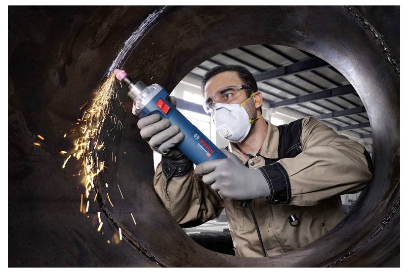 Osoba ubrana w odzież ochronną używa niebieskiego ręcznego elektronarzędzia do szlifowania metalu, podczas gdy w przemysłowym otoczeniu lecą iskry.