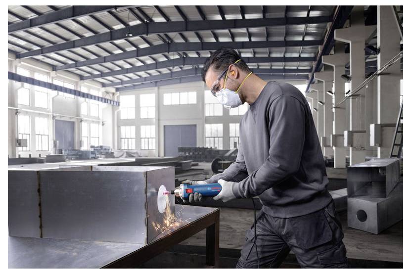 Osoba ubrana w sprzęt ochronny używa elektronarzędzia do cięcia metalu w przemysłowym warsztacie, a wokół miejsca cięcia lecą iskry.