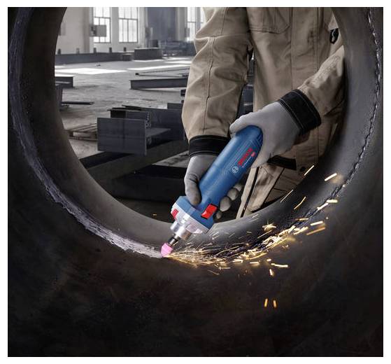 Osoba w warsztacie używa niebiesko-czerwonego ręcznego narzędzia elektrycznego do szlifowania wewnętrznej części dużej metalowej rury, wytwarzając przy tym snop iskier.