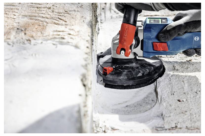 Robotnik budowlany używa elektronarzędzia do szlifowania ściany z cegły, tworząc przy tym pył. Narzędzie posiada czerwoną rączkę, a robotnik ma na rękach rękawice.