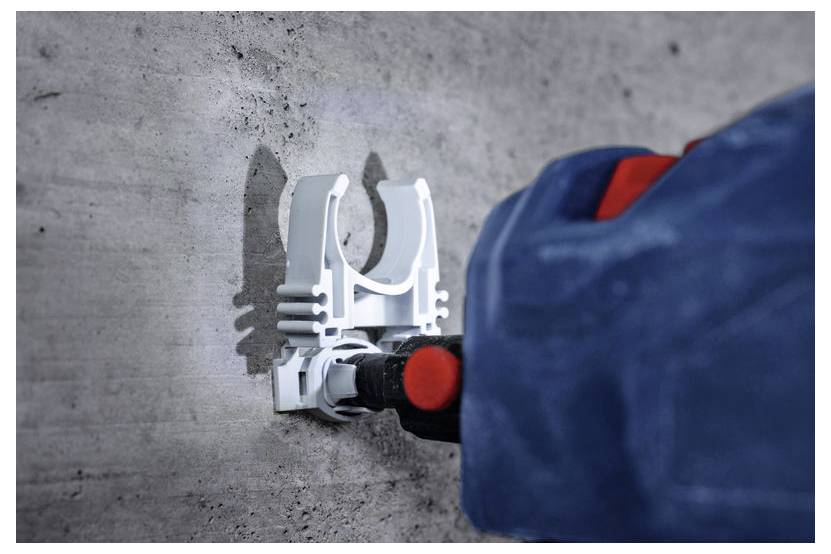 Ręka używająca wiertarki mocuje białą wspornikę do betonowej ściany. Wiertarka jest niebieska z czerwonymi akcentami, koncentrując się na solidnym zamocowaniu.