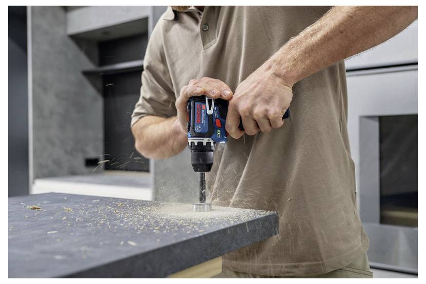 Osoba używa wiertarki bezprzewodowej, aby wywiercić otwór w blacie kuchennym, przy czym wokół rozrzucane są wióry.
