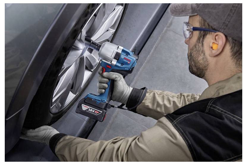 Osoba ubrana w odzież ochronną używa bezprzewodowego klucza udarowego do dokręcenia lub poluzowania nakrętek mocujących na kole samochodu w warunkach warsztatowych.