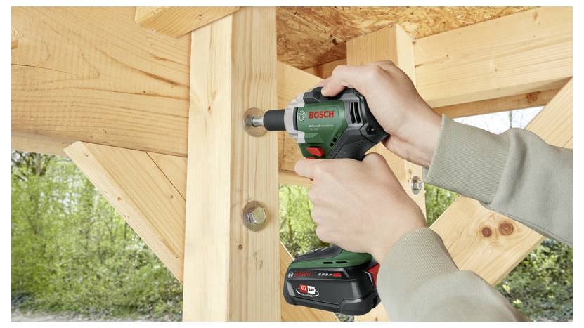 Osoba używa wiertarko-wkrętarki Bosch do wkręcenia śruby w drewnianą konstrukcję, prezentując prace stolarskie w plenerze.