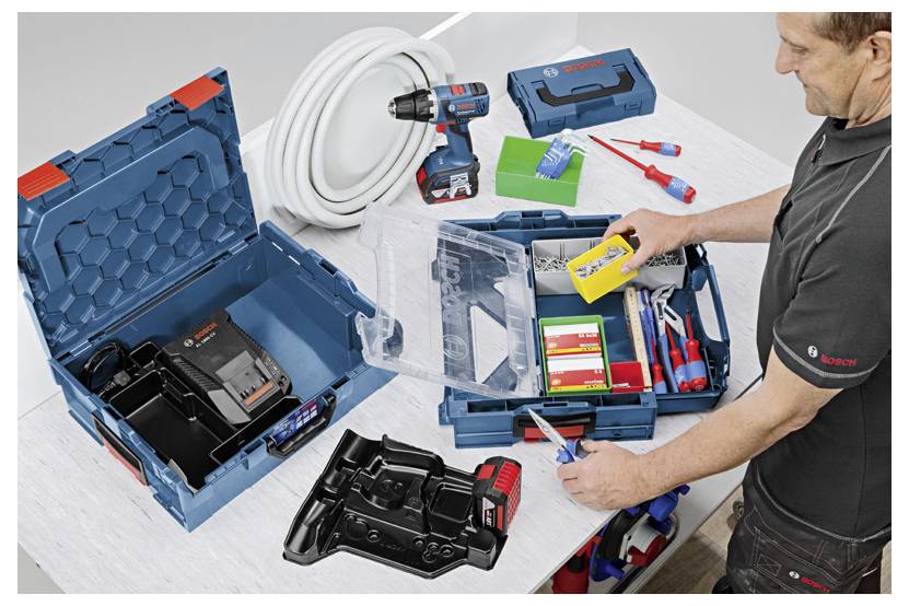 Osoba organizuje skrzynkę narzędziową, w której znajduje się akumulatorowa wiertarka, różne wiertła, ładowarka do akumulatora i inne narzędzia na stole warsztatowym.