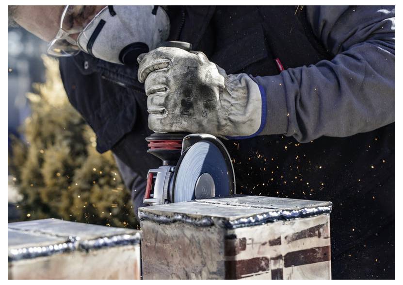 Osoba w ochronnych rękawicach i okularach używa szlifierki kątowej, wytwarzając iskry podczas cięcia metalu.