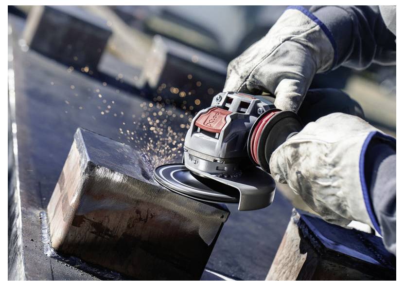 Osoba w rękawicach używa elektrycznej szlifierki na metalowej powierzchni, tworząc snop iskier. Zdjęcie koncentruje się na precyzyjnym ruchu narzędzia.