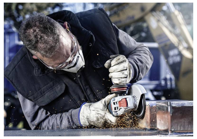 Osoba ubrana w odzież ochronną używa szlifierki kątowej do cięcia metalu, a pomarańczowe iskry wylatują, gdy narzędzie styka się z powierzchnią.