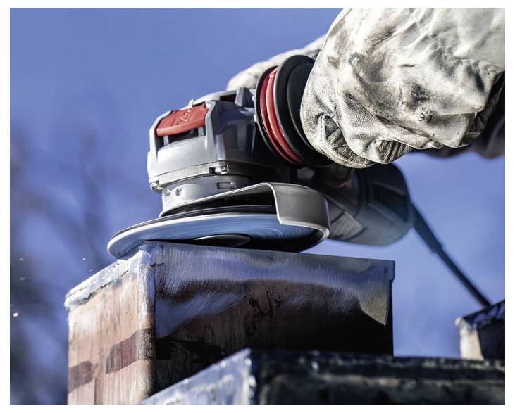 Osoba używająca szlifierki kątowej na metalowej powierzchni na zewnątrz, ubrana w odzież ochronną; widoczne są iskry, w tle niebo.