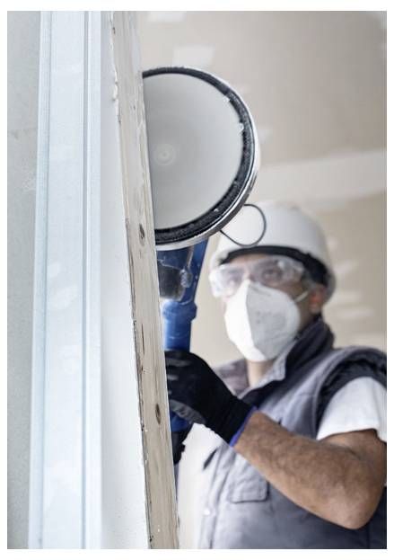 Robotnik budowlany w odzieży ochronnej używa piły tarczowej do przycinania deski drewnianej, koncentrując się na precyzji i bezpieczeństwie.