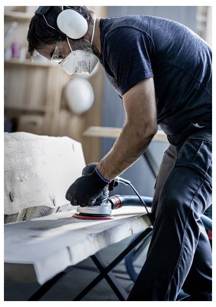 Osoba w stroju ochronnym szlifuje drewnianą powierzchnię w warsztacie.