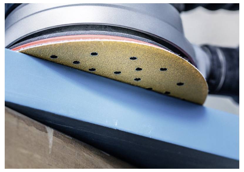 'Zbliżenie na szlifierkę z okrągłą tarczą szlifierską wygładzającą drewnianą powierzchnię pomalowaną na niebiesko.'