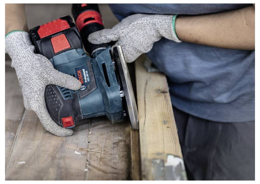 Osoba używa ręcznej szlifierki elektrycznej na drewnianej powierzchni, nosząc ochronne rękawice dla bezpieczeństwa.