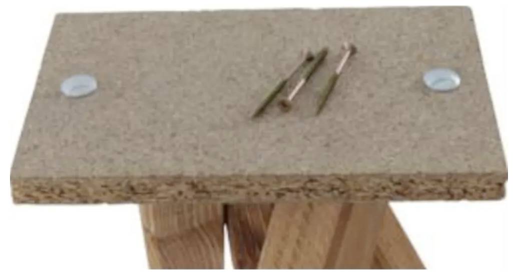 Prostokątna tablica korkowa z dwoma gwoździami i dwoma śrubami na górze, wsparta na dwóch drewnianych nogach.