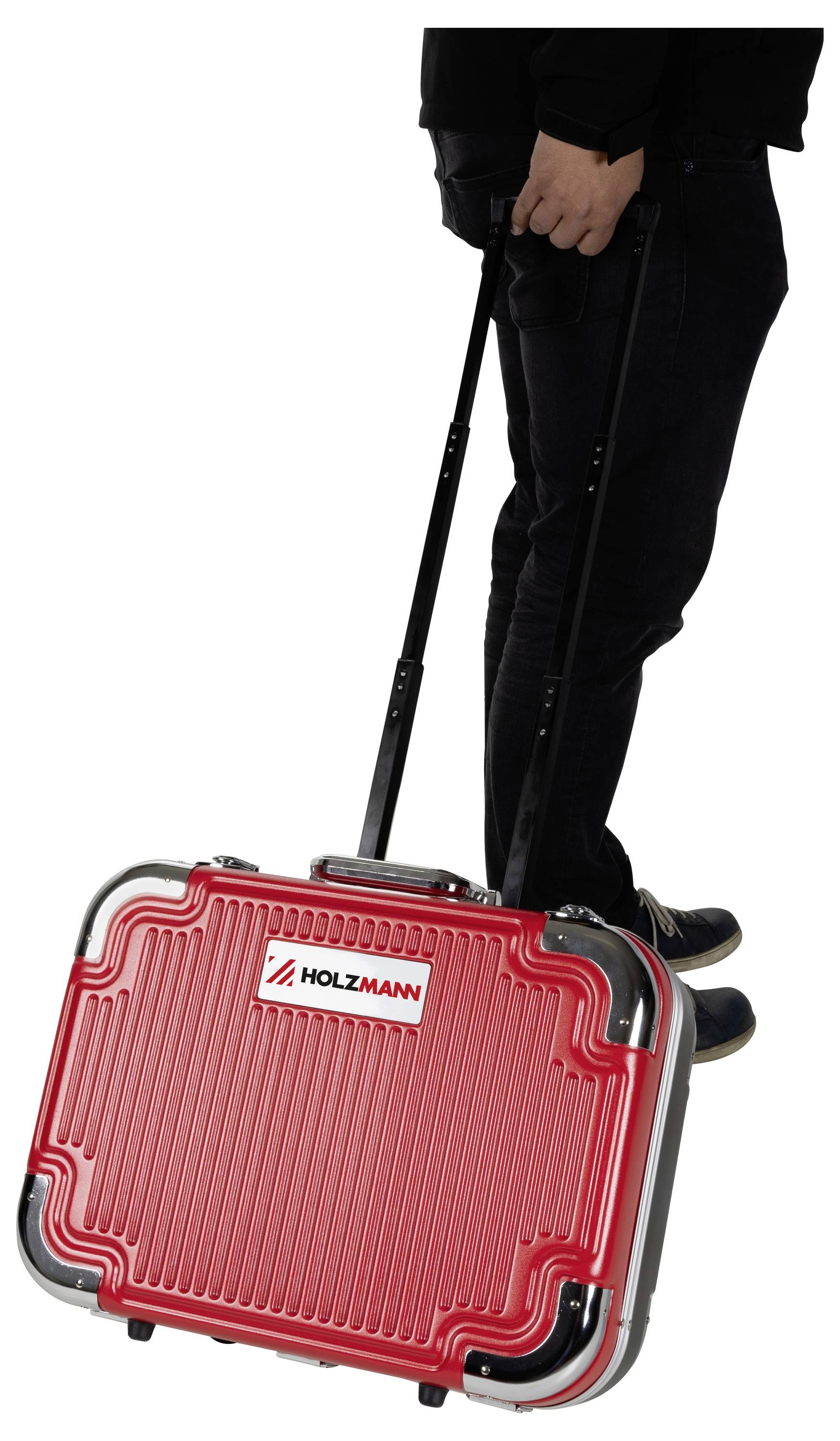 Osoba ubrana na czarno ciągnie czerwoną walizkę marki HOLZMANN z wysuwaną rączką.