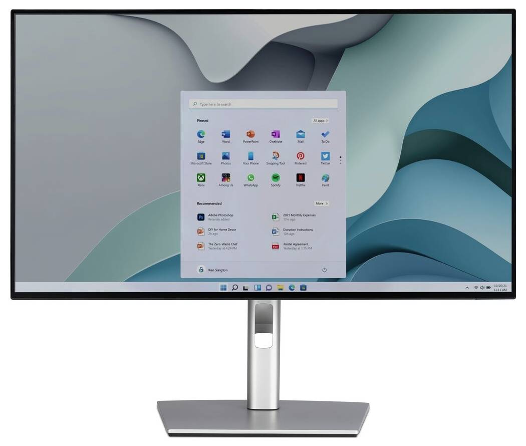 Monitor komputerowy wyświetlający ekran główny systemu Windows 11 z różnymi ikonami aplikacji i paskiem wyszukiwania na tle abstrakcyjnym w odcieniach niebieskiego i szarego.