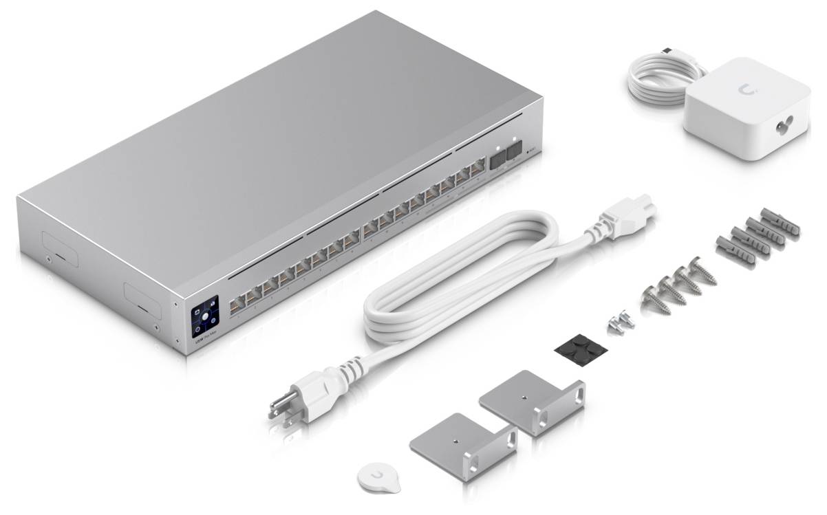 Zestaw urządzeń sieciowych obejmujący srebrny switch z wieloma portami, przewód zasilający, uchwyty montażowe oraz wkręty, prezentowany na białej powierzchni.