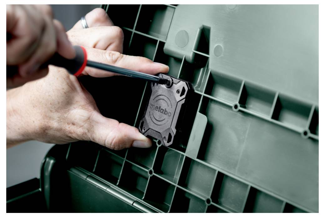 Osoba używa wkrętaka, aby przymocować małą czarną część oznaczoną napisem 'Metabo' na zielonej plastikowej powierzchni z wzorem kratki.