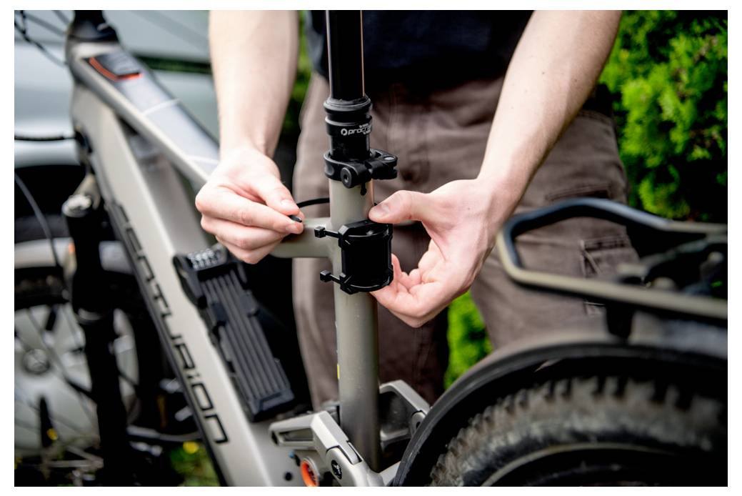 Osoba regulująca zacisk siodełka szarego roweru. Ręce dokręcają śrubę na zacisku, co wskazuje na czynności konserwacyjne lub przygotowanie do jazdy.