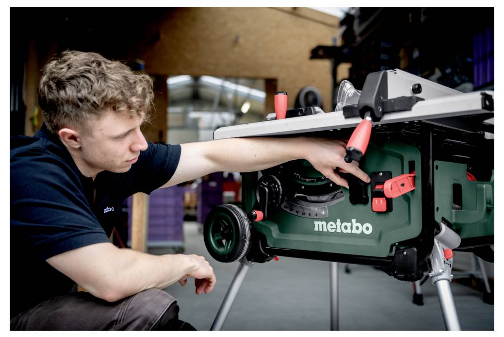 Osoba regulująca piłę stołową Metabo wewnątrz warsztatu, koncentrująca się na sterownikach urządzenia z ostrożnym wyrazem twarzy.