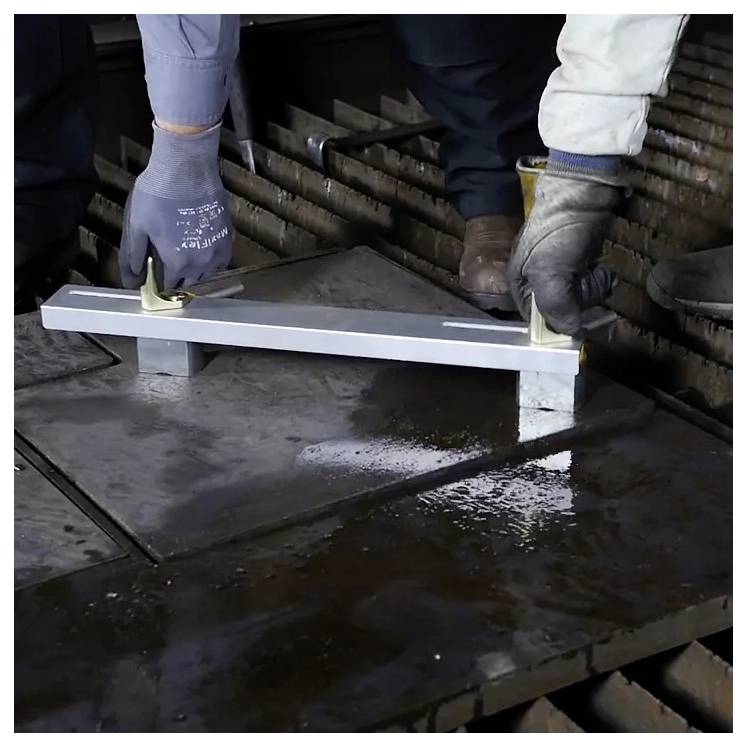 Dwóch robotników używa metalowego narzędzia do regulacji ciężkich stalowych płyt, przygotowując je do cięcia lub spawania w środowisku przemysłowym.