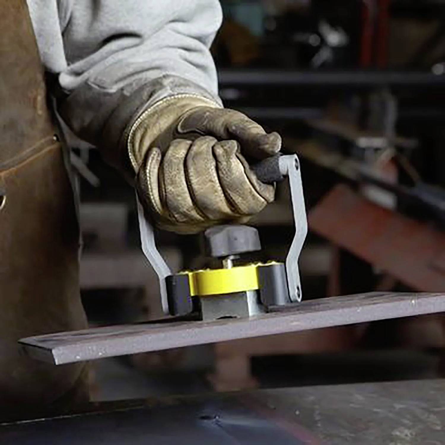 Pracownik w rękawicach używa podnośnika magnetycznego do przenoszenia płyty metalowej w środowisku przemysłowym.