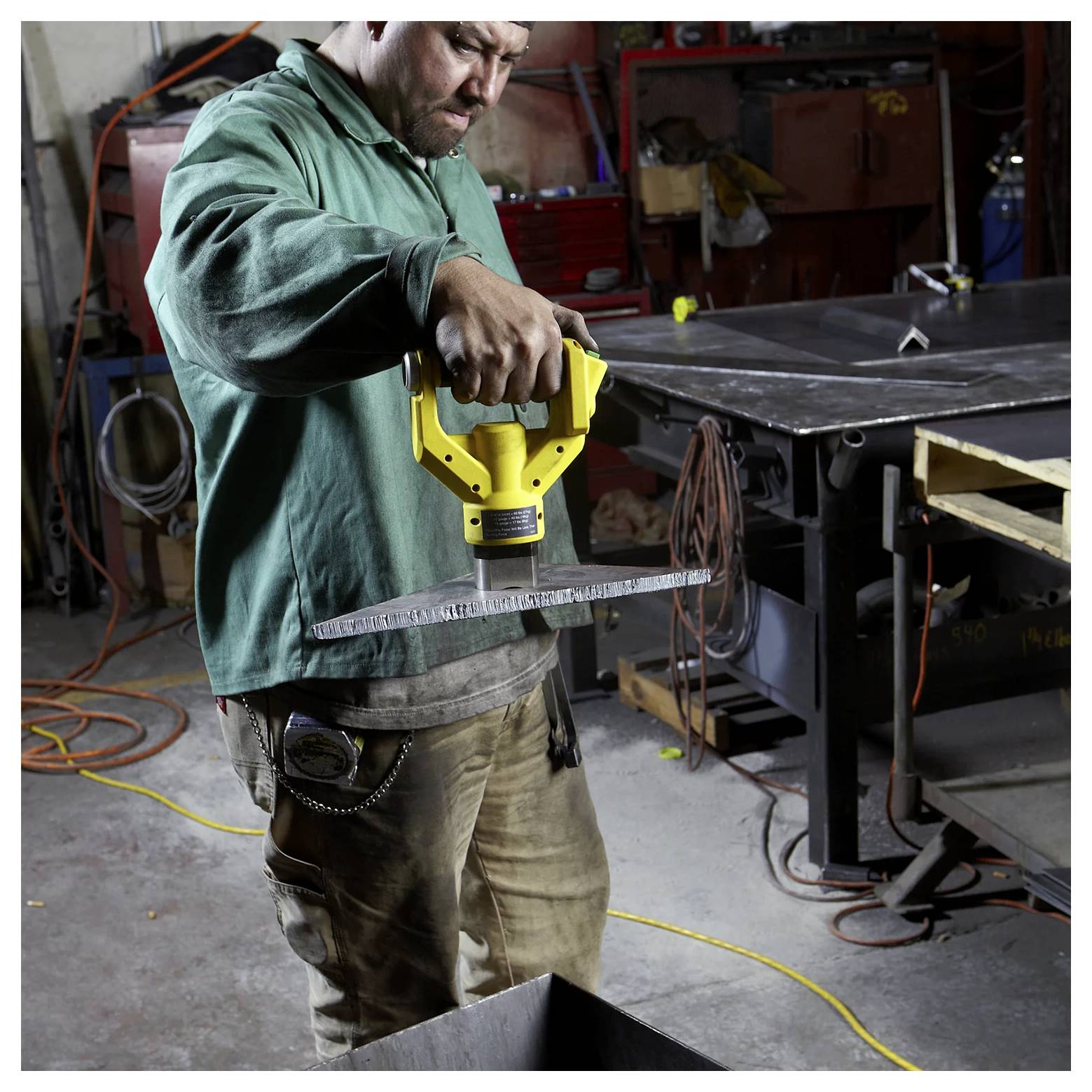 Osoba w warsztacie używa narzędzia pomiarowego do sprawdzania wymiarów kawałka materiału, otoczona narzędziami i sprzętem.