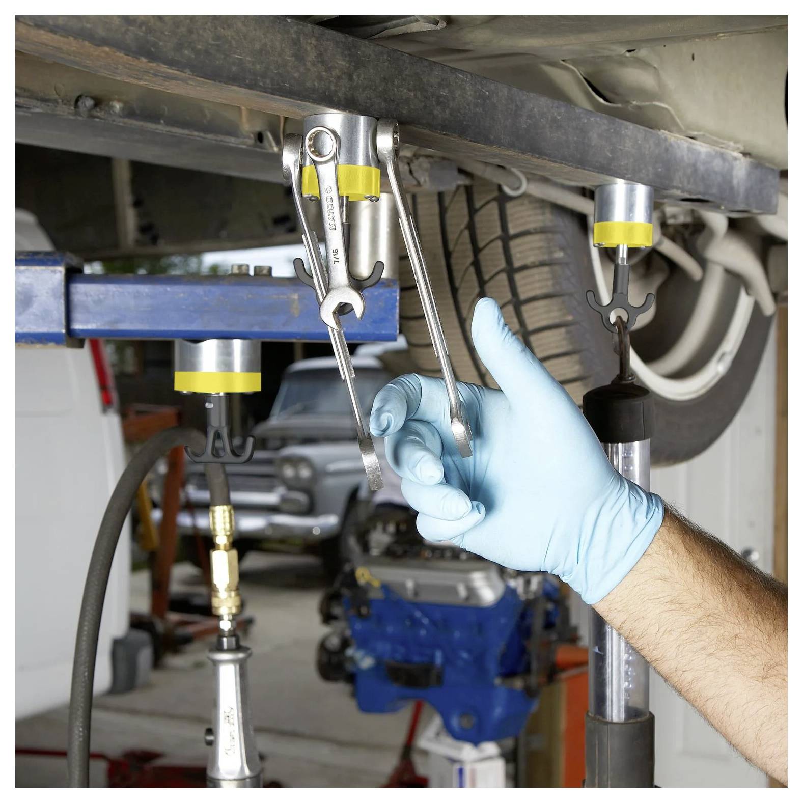 Osoba nosząca niebieską rękawicę używa klucza do dokręcenia śruby na oponie samochodu zabezpieczonego podporami w warsztacie samochodowym.