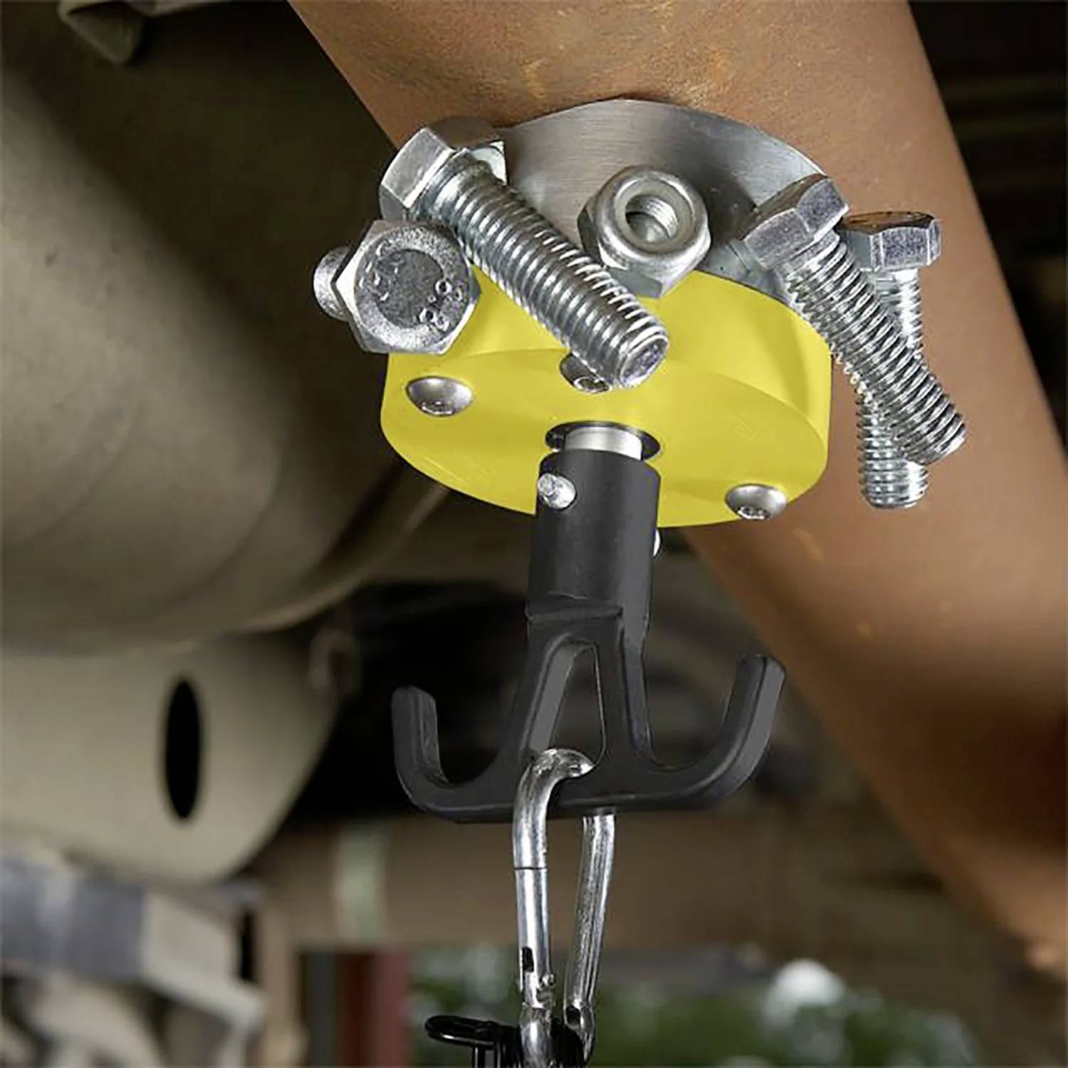 Narzędzie jest przymocowane do wiszącej rury wydechowej samochodu za pomocą żółtego zacisku z czterema metalowymi śrubami, podtrzymując rurę podczas prac naprawczych.